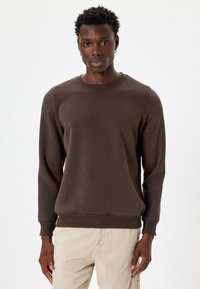 Sudadera marrón hecha de una tela suave, con cuello redondo, mangas largas, puños acanalados y un dobladillo recto. Diseño simple y sin costuras.