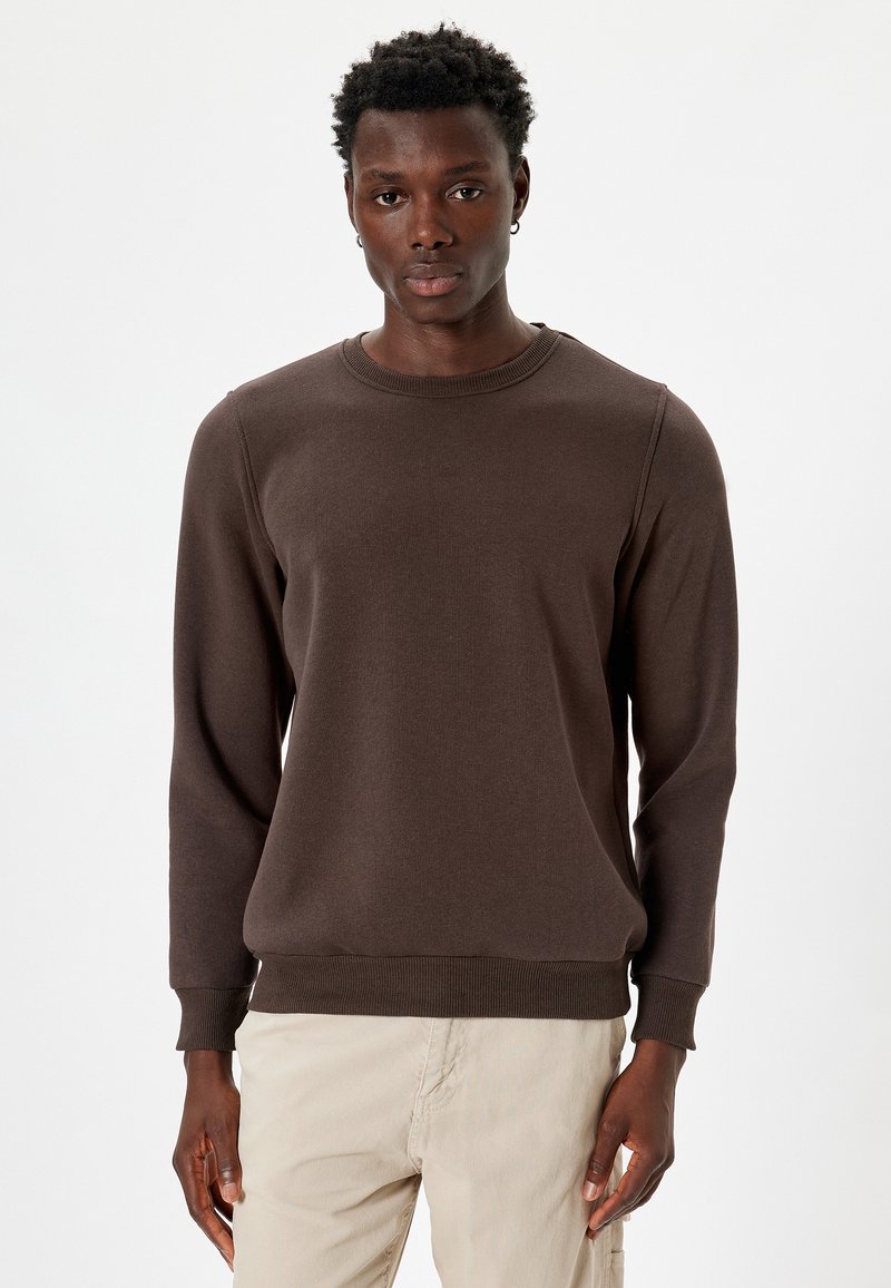 Sudadera marrón hecha de una tela suave, con cuello redondo, mangas largas, puños acanalados y un dobladillo recto. Diseño simple y sin costuras.