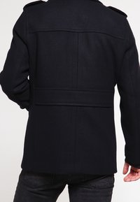 Mörkblå ulljacka med strukturerad passform, bakre söm och axelklaffar; har en ren, minimalistisk design.