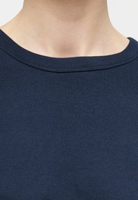 Gros plan d'une personne portant un pull à col rond côtelé bleu marine, montrant le col et la partie supérieure de la poitrine.