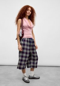 Pink sleeveless top with draped neckline, plaid culottes in navy and cream, gray shoes, white ankle socks, carrying a burgundy bag.
