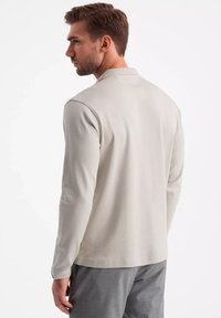 Helles graues Polohemd mit langen Ärmeln und Kragen, aus weichem Stoff gefertigt, mit glatter Textur und minimalistischem Design.