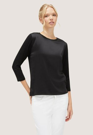 Top negro de manga tres cuartos con una textura suave y escote redondo, combinado con pantalones blancos. Diseño sencillo sin patrones visibles.