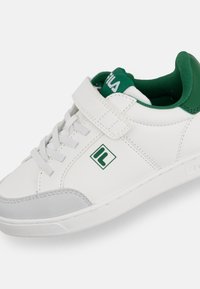 Sneaker bianco e verde con lacci e cintura in Velcro, punta grigia, colletto imbottito e logo "IL" di lato.
