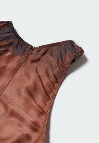 Nahaufnahme von braunem und dunklem Batikstoff ohne Ärmel mit elastischen Kanten und einem kleinen Reißverschluss auf hellem Hintergrund.