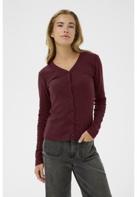 Burgundy cardigan med v-ringning, långa ärmar och knappstängning fram, gjord av mjukt, strukturerat tyg. Matchas med mörkgrå jeans.