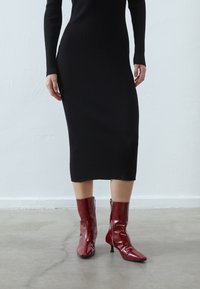 Robe en maille côtelée noire à manches longues, associée à des bottines rouges brillantes avec un bout pointu et une fermeture éclair latérale.