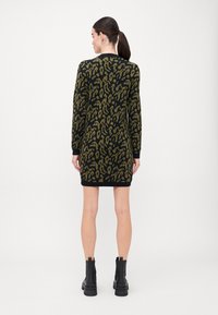 Strikket kjole med svart bunn som har et grønt leopardmønster, ribbede mansjetter og rett silhuett, parret med svarte ankelstøvler.