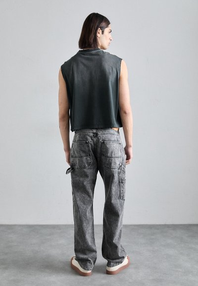 Sleeveless dark green cropped top, gray cargo jeans with multiple pockets, visible stitching, and beige platform sneakers. Plain background.