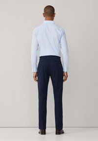 Camisa azul claro abotonada con mangas largas, combinada con pantalones azul marino. La camisa tiene un cuello clásico y los pantalones cuentan con bolsillos traseros.