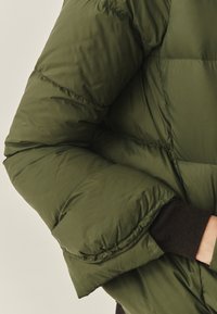 Puffjakke i mørkegrøn, med et quiltet design, tyk isolation og elastiske sorte manchetter for varme og komfort.