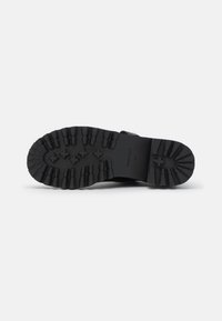 Suela de goma negra con surcos profundos y ranuras para tracción; presenta patrones texturizados y detalles de marca en el costado.