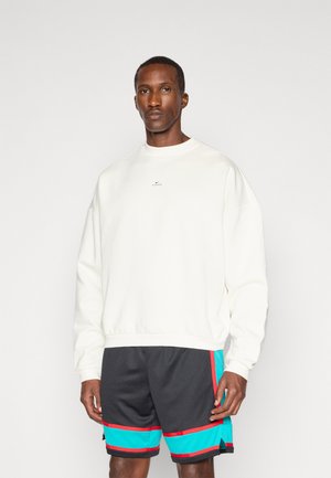 White sweatshirt with a crew neckline and slight drop shoulders, paired with black shorts featuring turquoise and red accents.