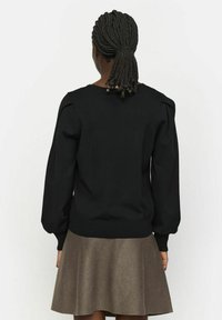 Maglione nero con maniche a sbuffo e bordo a coste, abbinato a una gonna marrone a campana. Il maglione presenta un colletto rotondo e un tessuto testurizzato.