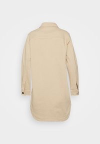 Veste en coton beige avec col, manches longues et poignets boutonnés. Ourlet arrondi avec fentes sur les côtés pour plus de confort.