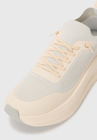 Helebeige tennis jalan, millel tekstureeritud võrkvest, lamedad paelad ja pehmendatud tald. Diskreetne aksent koor- ja heleda halli värviga.