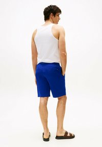Pantaloni corti blu royal con elastico in vita, due tasche posteriori e una texture liscia. Indossati con una canotta bianca e sandali marroni.