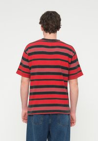 Κοντομάνικο κόκκινο μπλουζάκι με οριζόντιες μαύρες και γκρι ρίγες. Διαθέτει στρογγυλή λαιμόκοψη και άνετη εφαρμογή. Το ύφασμα φαίνεται υφασμάτινο.