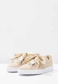 Sneaker in suede beige con lacci in satin spessi e suole in gomma bianca. Presenta una suola texturizzata e un branding minimale.