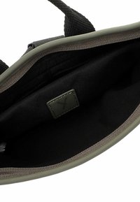 Interno nero di una borsa con rifiniture verde oliva, caratterizzato da una superficie texturizzata e una piccola etichetta scura con un logo.