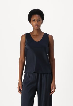 Marineblaue ärmellose Bluse aus glattem, glänzendem Stoff mit rundem Ausschnitt und lockerer Passform, kombiniert mit dunklen, gefalteten Hosen.