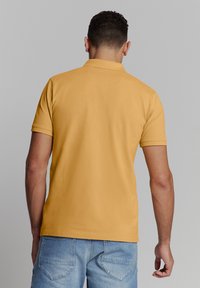 Geel katoenen poloshirt met een kraag, korte mouwen en achternaaddetails, gecombineerd met lichtblauwe denim shorts.