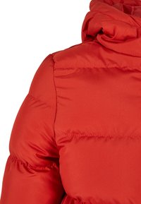 Rød puff jakke med høy krave, sydd seksjoner for isolasjon, og glatt, shiny stofftekstur. Synlige sømdetaljer på ermet.