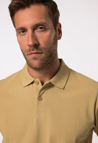 Béžové polo tričko s klasickým límečkem a dvouknoflíkovou légou. Bavlněný materiál s texturovaným povrchem, přiléhavý střih a krátké rukávy.