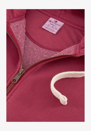 Bordowa bluza z kapturem zapinana na zamek, z miękkim, polarowym wykończeniem. Posiada kremowy sznurek i metalowy zamek. Wewnątrz widoczna metka rozmiaru.