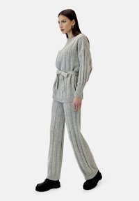 Suéter gris de punto y pantalones a juego con rayas verticales; presenta un cinturón en la cintura, mangas largas y puños acanalados.