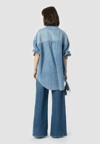 Camicia oversize in denim blu chiaro con maniche arrotolate, orlo curvo e pantaloni in denim a gamba larga abbinati. Tessuto morbido, vestibilità casual.