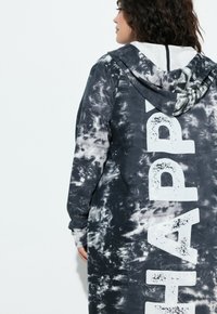 Zwart-witte tie-dye hoodie met het woord "HAPPY" in vetgedrukte witte letters op de achterkant. Heeft een capuchon met trekkoorden en lange mouwen.