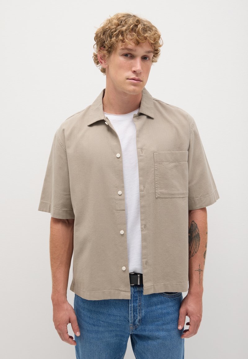 Chemise à manches courtes, couleur kaki, à boutons, fabriquée en tissu léger, avec une poche poitrine et une coupe décontractée, assortie à un jean bleu.
