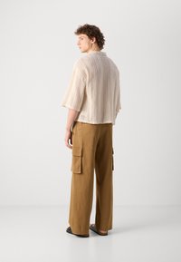 Beige kötött, rövidujjú ing, laza szabású, barna cargo nadrággal párosítva, amely oldalzsebekkel és egyenes szárú kialakítással rendelkezik.