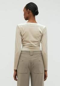 Långärmad beige topp gjord av slät tyg, i kombination med högmidjade beige byxor med två bakfickor och knappryck.