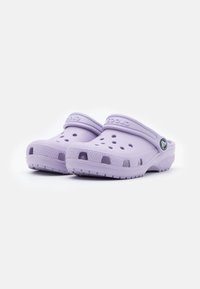 Zoccoli Crocs di un leggero colore viola con fori di ventilazione, una suola testurizzata e una cinghia. Materiale liscio con una forma arrotondata ed ergonomica.