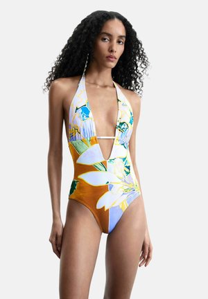 Kobieta z długimi kręconymi włosami ubrana w jednoczęściowy strój kąpielowy z wiązaniem na szyję, z dużymi kwiatowymi wzorami w białych, niebieskich, zielonych i pomarańczowych tonacjach.
