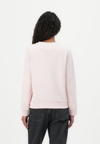 Lichtroze sweatshirt met ronde hals en lange mouwen. Kenmerkt zich door ribgebreide manchetten en onderrand, een soepele textuur en een relaxte pasvorm.