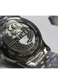 Stainless steel watch back featuring a globe design, engraved "Timex," and "The Chicago Collection," with a silver metal strap.