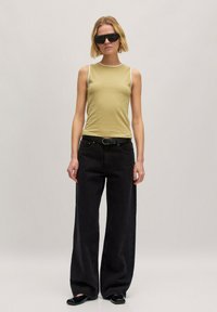 Aansluitend olijfkleurig tanktop met witte afwerking, gecombineerd met hooggetailleerde zwarte wijde jeans en zwarte platte schoenen. Model draagt zwarte zonnebril en oorbellen.