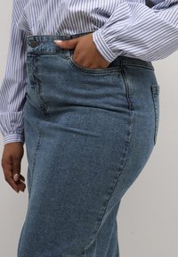 Hoge taille denim jeans in medium blauw met een gladde textuur. Beschikt over een voorzak en een metalen knoop, gecombineerd met een gestreepte lange mouw shirt.