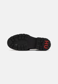 Semelle en caoutchouc noire de sneaker avec un logo "HU" rouge audacieux. Présente un design de semelle texturée pour l'adhérence et la durabilité. Talon plat et rectangulaire.
