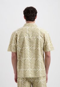 Korteblouse in licht olijfgroen met een wit bloemmotief, gemaakt van textuuroverweefde stof, met een ontspannen pasvorm en een ingesneden kraag.