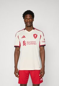 Liverpool FC tähistab kooriva värvi ja punaste aktsentidega, millel on logo ja sponsori tekst. Tootes on V-kaelused ja punased lühikesed püksid Adidas logoga.