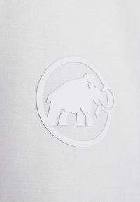 Hvidt stofoverflade med et hævet, cirkulært logo med et stiliseret elefantdesign, glat tekstur og rene konturer.
