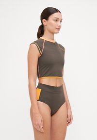 Barna crop top narancs és zöld díszítéssel, magas derekú bikinifelsővel párosítva, narancssárga oldalsó panellel. Simaság jellemzi.