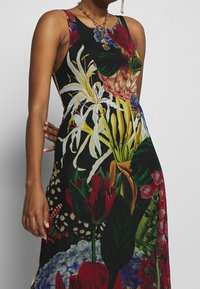 Kwiatowa sukienka na czarnym tle, z jaskrawymi wzorami żółtych, czerwonych i zielonych kwiatów. Bezrękawowy krój z dopasowaną talią.