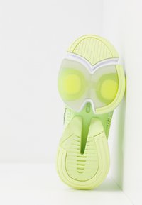 Kengän pohja, jossa on läpikuultava vihreä ja keltainen väriyhdistelmä, teksturoituja kuvioita ja erottuva leikkausmuotoilu, jossa on pyöreitä aksentteja.