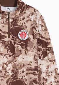 Rudas megztinis su užtrauktuku, su kamufliažo raštu šviesiomis ir tamsiomis atspalviais. FC St. Pauli logotipas ir "1910" detalė priekyje.