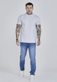 Gray short-sleeve t-shirt with a round neckline, paired with light blue denim jeans and white sneakers, displayed on a model.
